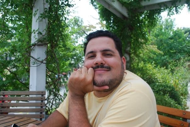Juan resting his chin on his hand at an outdoor table