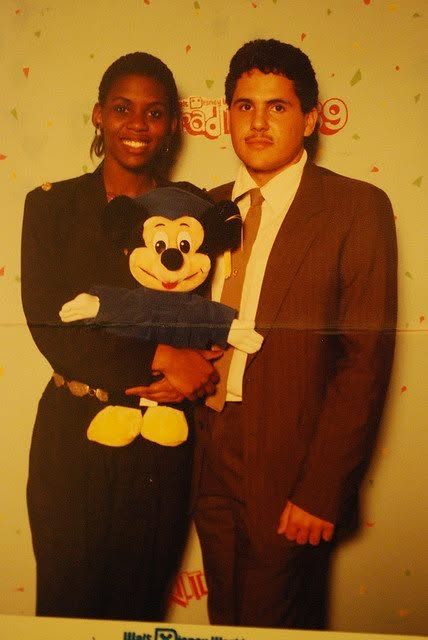 Juan in a brown suit next to a woman holding a Mickey Mouse plush at Grad Nite '89